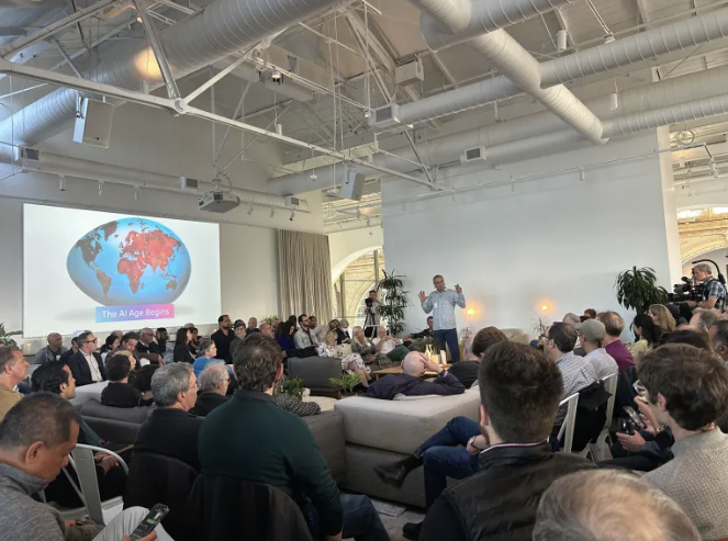 A speaker addresses a seated audience in a modern conference room. A slide showing a world map with "The AI Age Begins" is projected behind him.